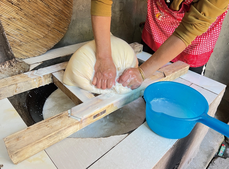 母亲熟练地按压豆腐包，将豆浆挤压而出